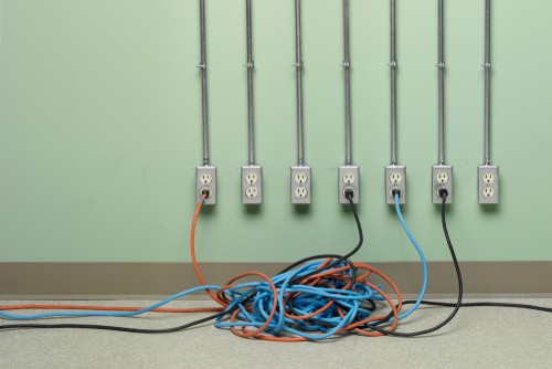 Blue Orange And Black Tangled Extension Cords Plugged Into Row