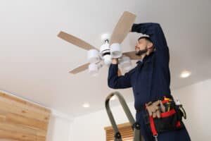 Electrician Repairing Ceiling Fan With Lamps Indoors.