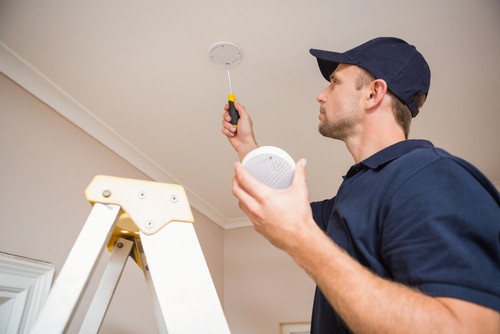 Handyman Installing Smoke Detector With Screwdriver On The Ceiling